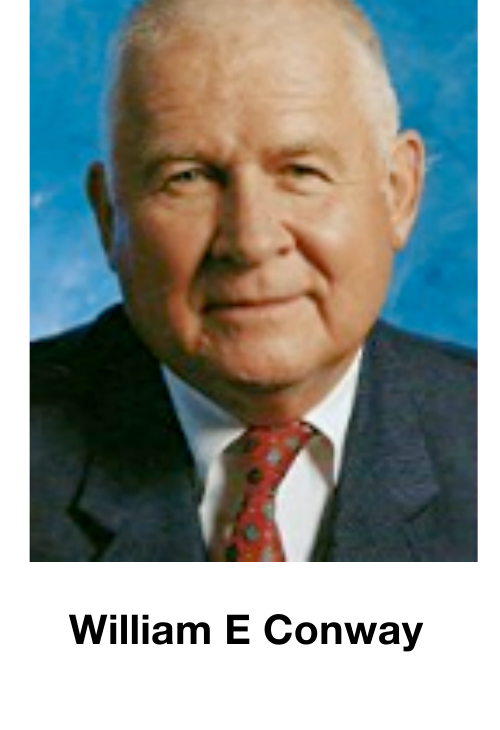 Portrait photograph of William E Conway in suit and tie against a blue background.